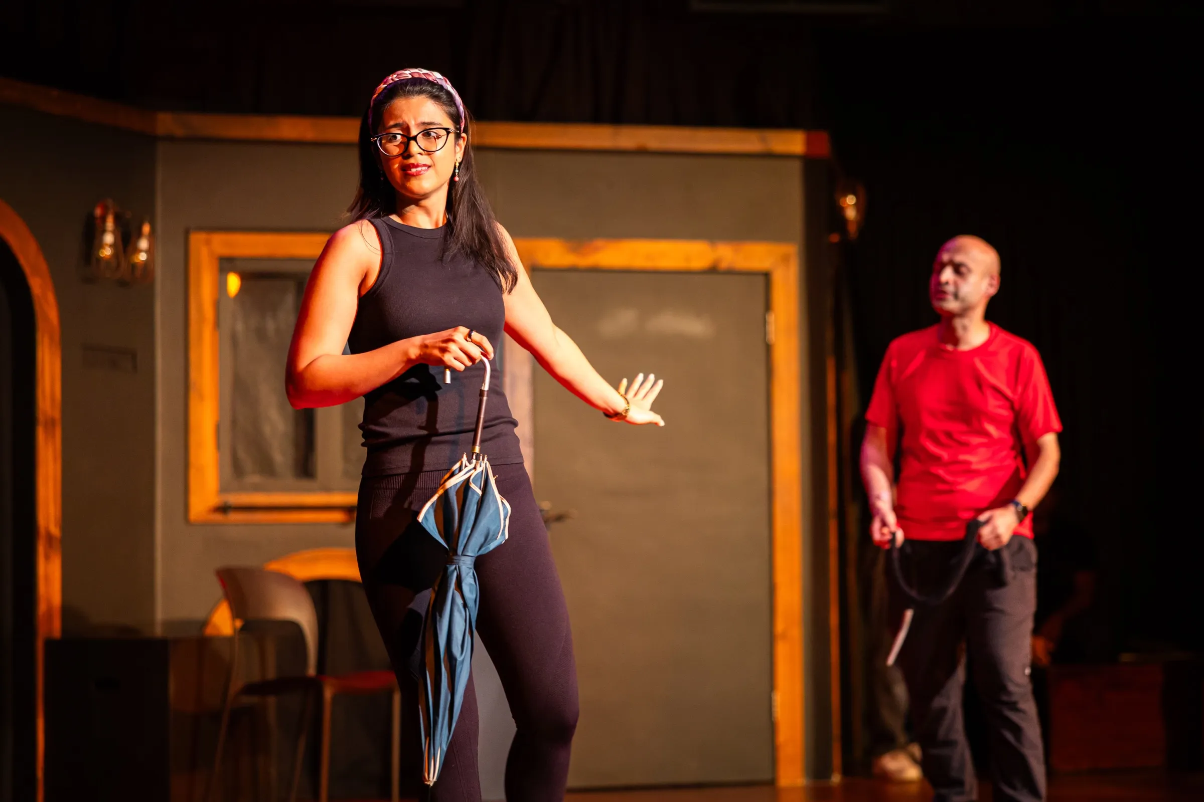 Two performers mid-scene on a warmly lit theatre stage set