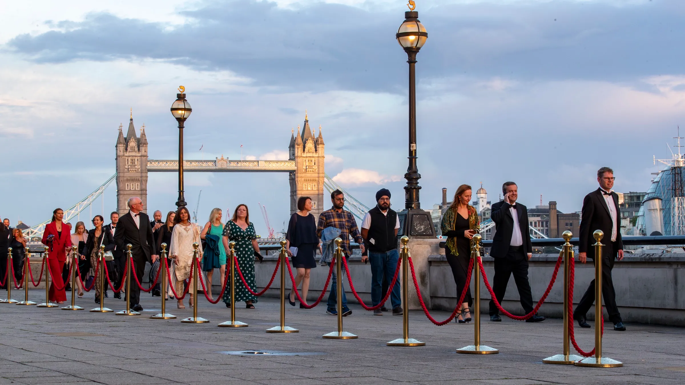 Guests arriving along a roped red carpet at dusk, with Tower Bridge and the Thames behind them